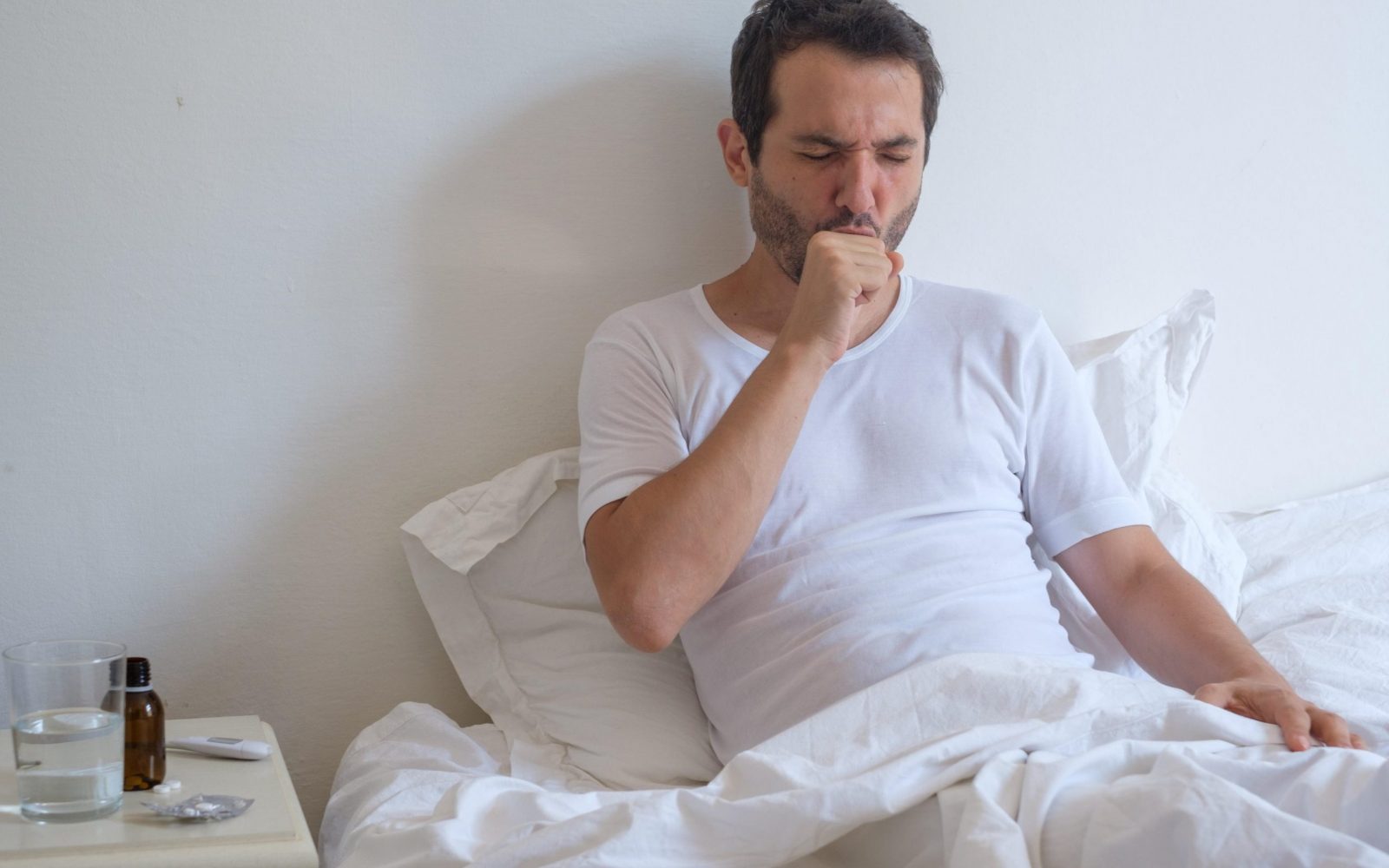 Moški leži v postelji in kašlja.