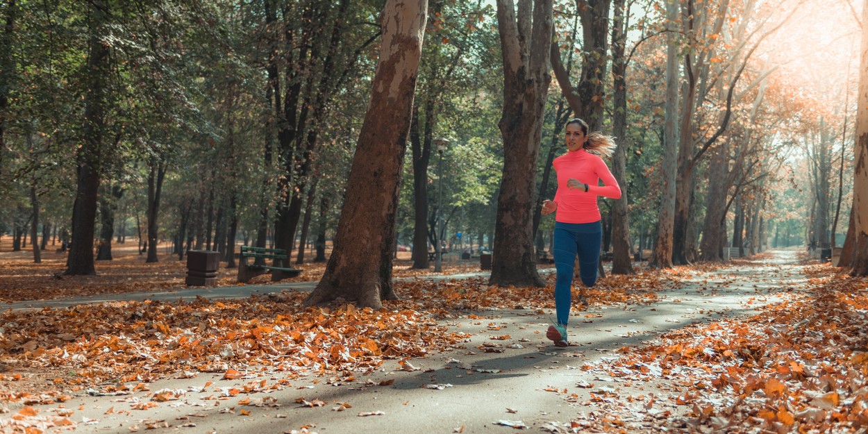 Ženska teče v jeseni, začetku pomladi, oblečena je v oranžen pulover in dolge tekaške pajkice