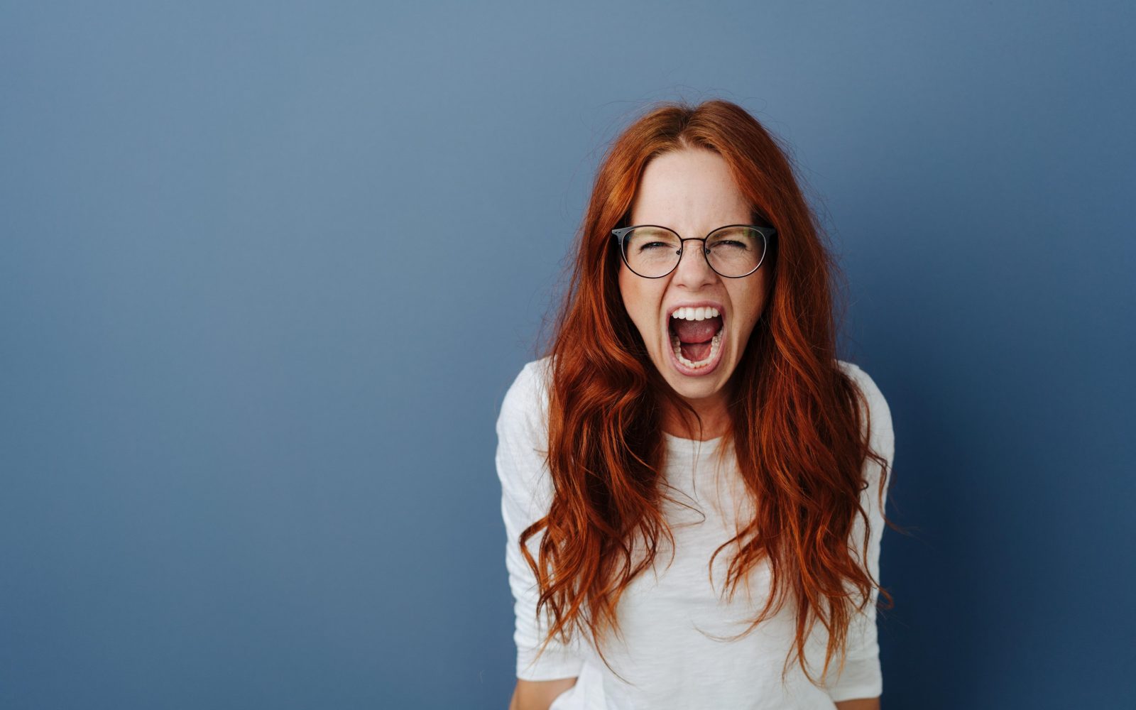 Ženska z rdečimi lasmi in očali kriči. Stres