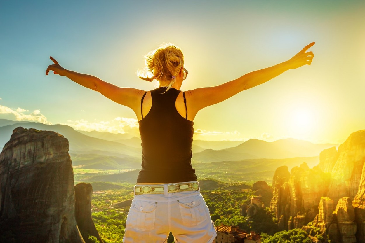 Ženska stoji v naravi, z razprtimi rokami, znak sreče in veselja