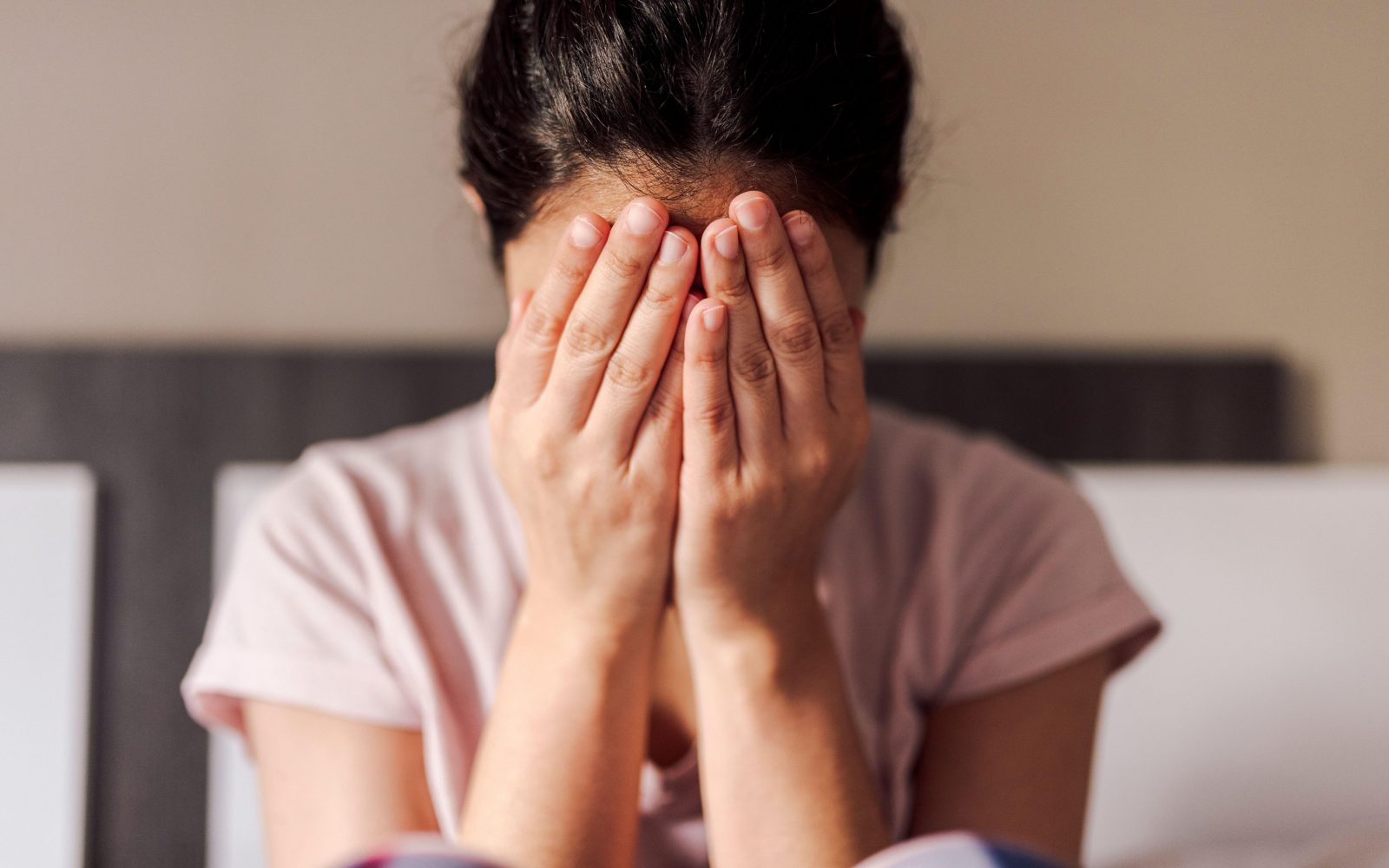 Ženska v stiski si z dlanmi pokriva obraz