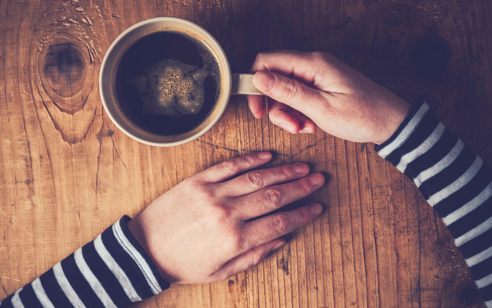 Človek drži roke na mizi, v eni roki ima skodelico kave