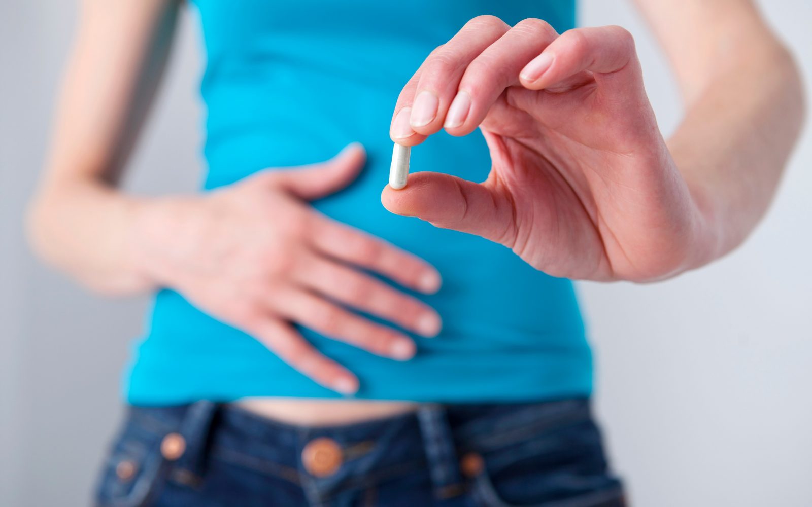 Ženska se drži za trebuh, v roki ima prehransko dopolnilo.