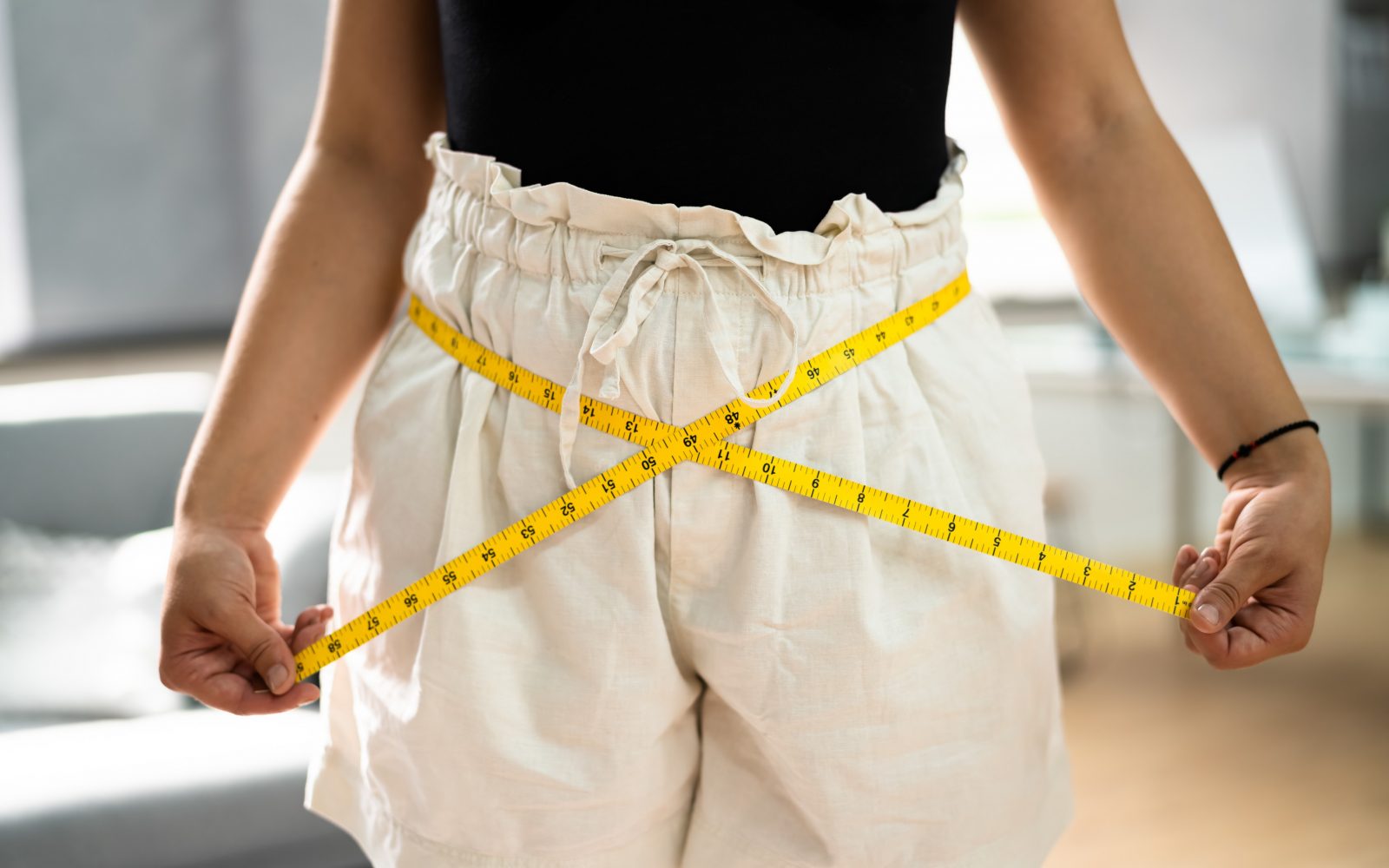 Hujšanje, ženska z belimi hlačami in šiviljskim metrom.