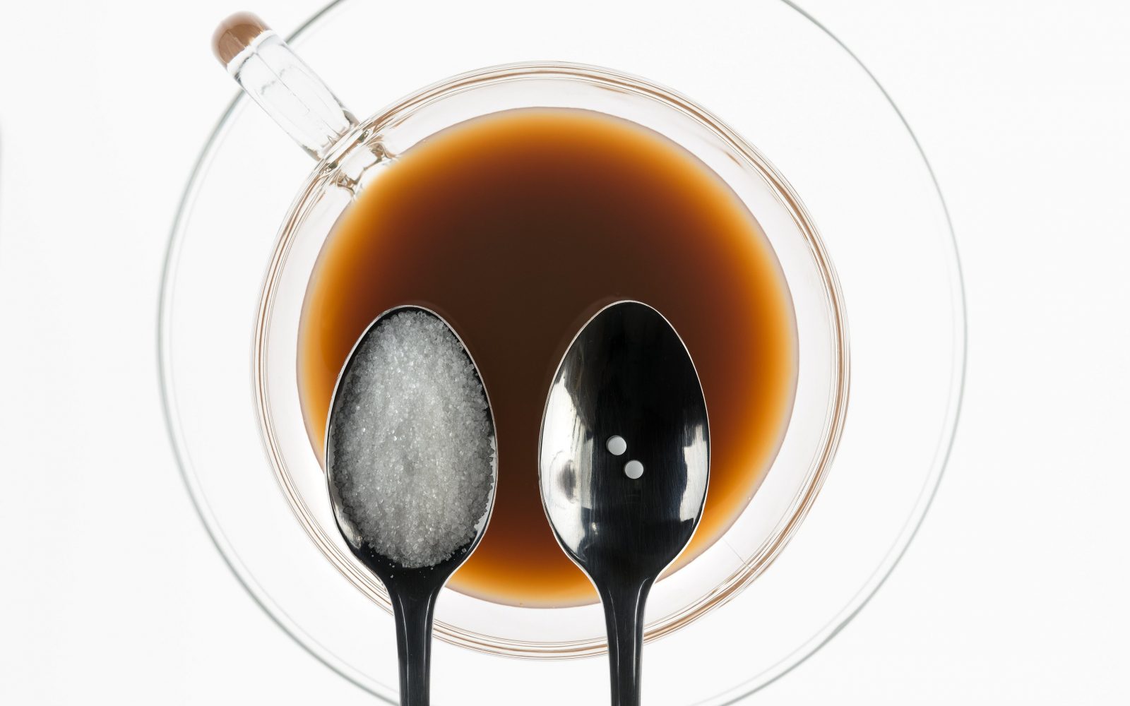 žlićka sladkorja in umetno sladilo nad skodelico kave