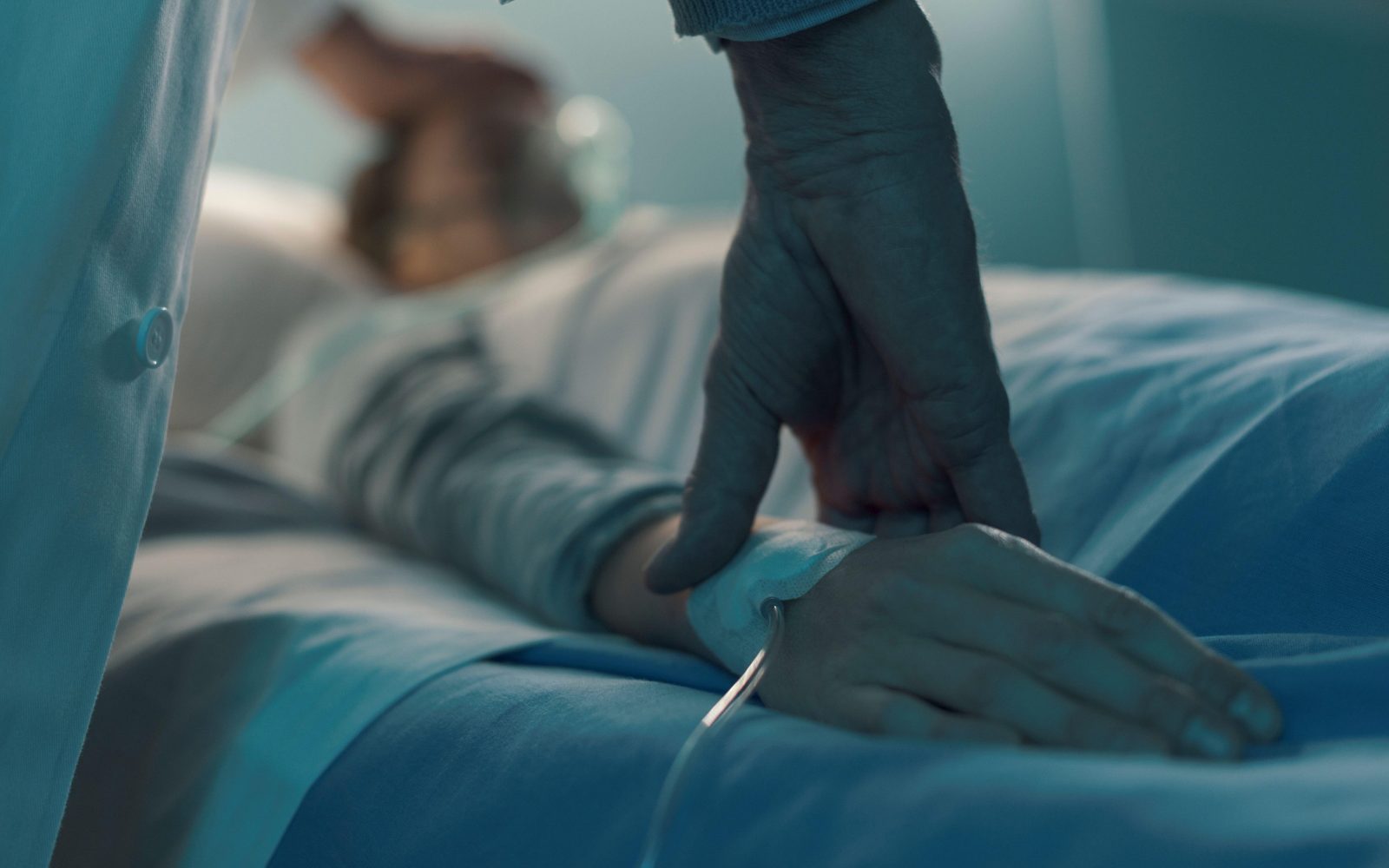 V postelji leži moški bolnih, ki za dihanje potrebuje kisikovo masko