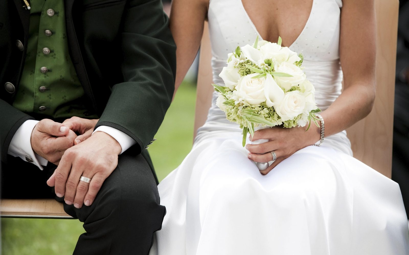 Nevesta v beli obleki s šopkom v rokah drži pod roko ženina