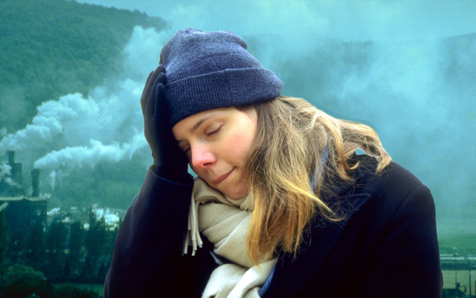 Ženska se drži za glavo, v ozadju se kadi iz dimnikov, koncept onesnaženega zraka