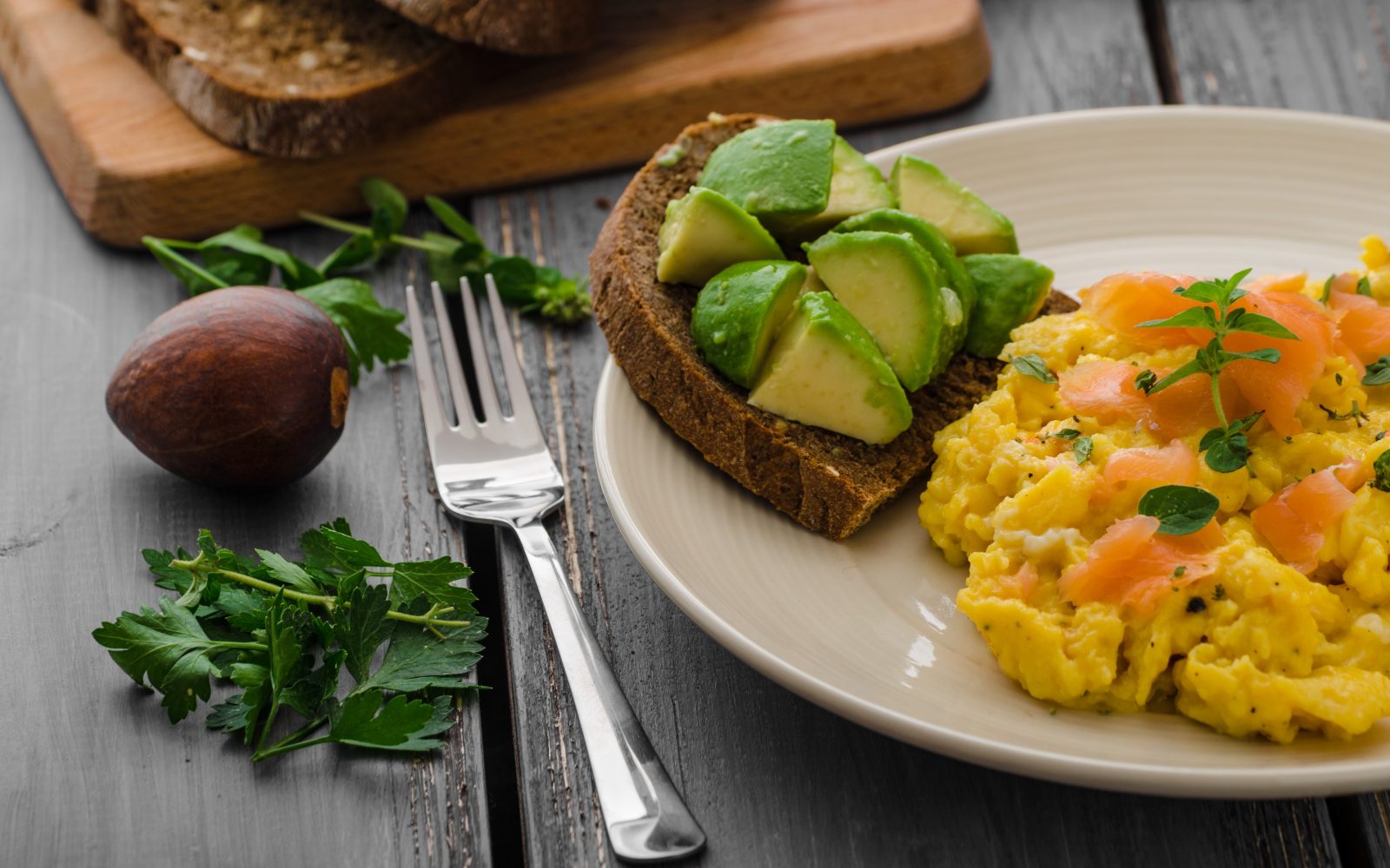 Na krožniku na mizi so zmešana jajca, poleg pa avokado na temnem kruhu