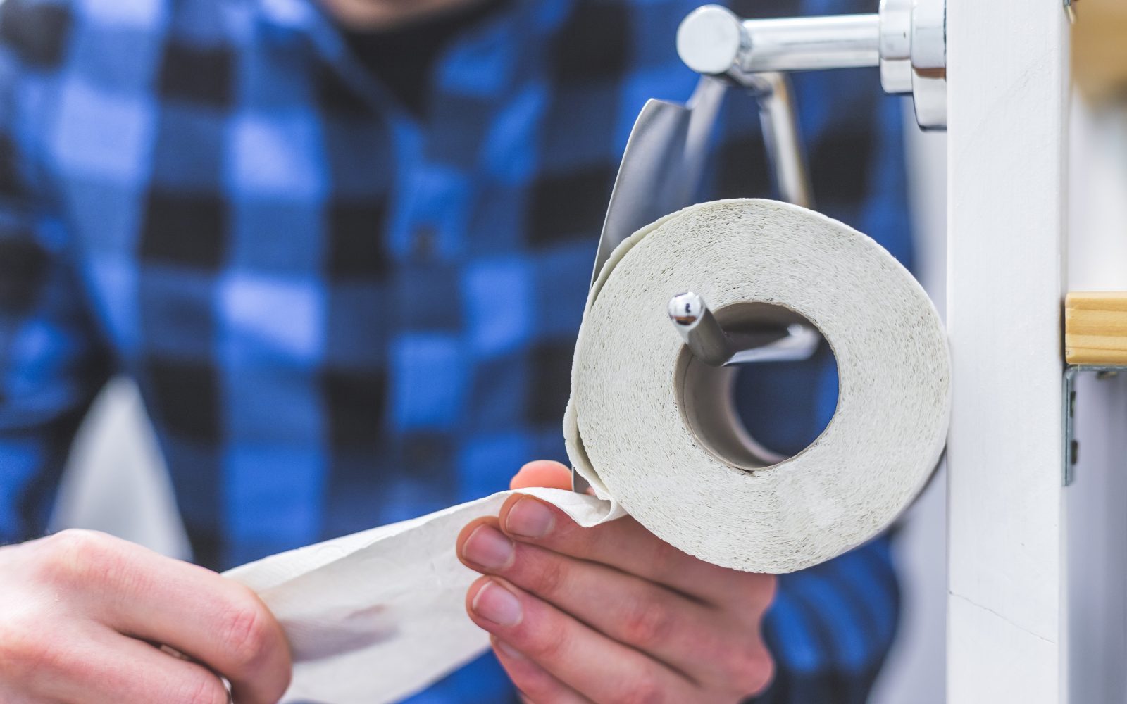 Moški v karirasti srajci sedi na stranišču, trga wc papir