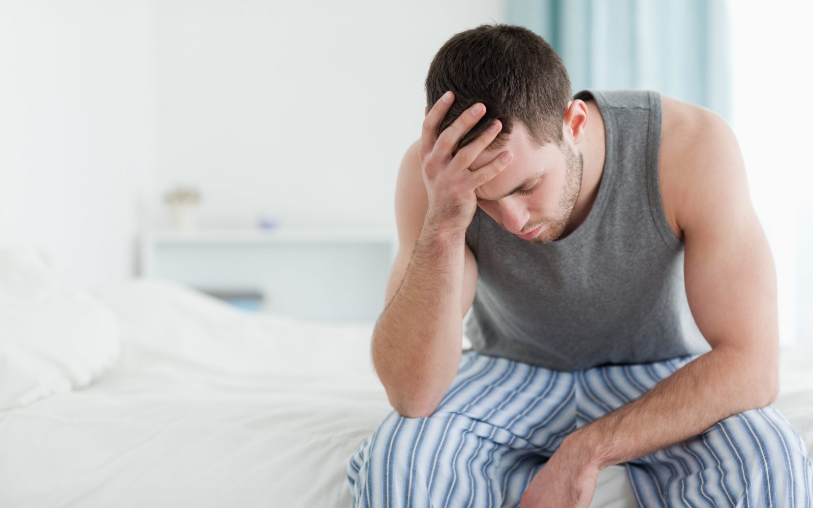 žalosten oziroma zaskrbljen moški sedi na postelji in se drži za glavo