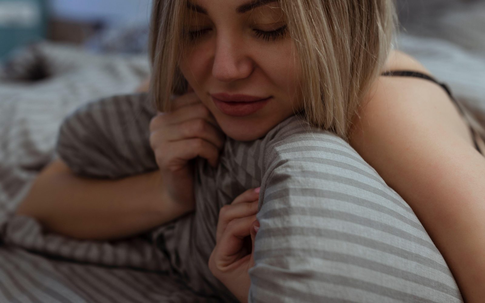 Ženska leži na postelji, objema blazino, se smehlja, ženska, orgazem, spolnost