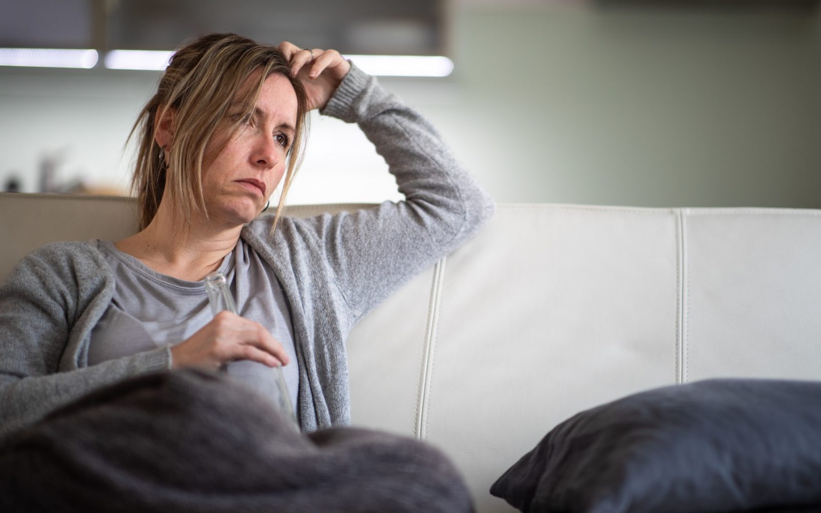 Ženska s steklenico alkohola v roki sedi na kavču