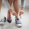 Fotografija prikazuje osebo, ki sedi na stolu in se preobuva iz modrih visokih pet v modre športne copate. Oseba zavezuje vezalke na športnih copatih, medtem ko ena visoka peta leži ob strani. Slika simbolizira udobje, prehod iz formalne v bolj sproščeno obutev in prilagodljivost. Primerna je za vsebino, povezano z modnimi nasveti, nasveti za udobno obutev, življenjskim slogom, udobjem med delom in prehajanjem iz službenega v prosti čas.