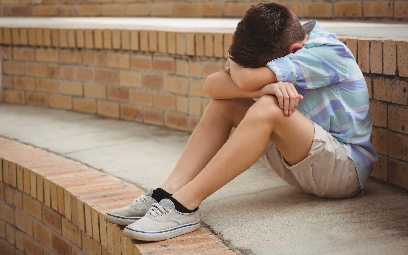 Žalosten najstnik sedi na tleh, glavo ima skrito med koleni