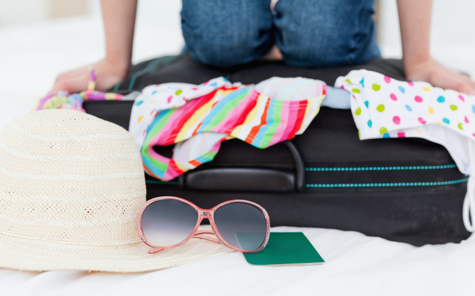 Oseba, ki pakira kovček z barvitimi oblačili, slamnikom, sončnimi očali in potnim listom..