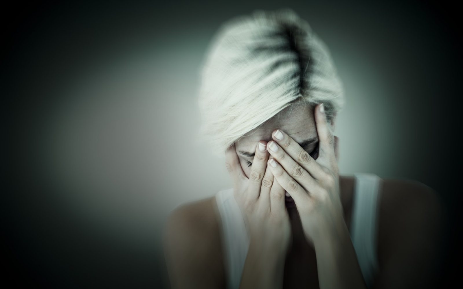Ženska v stiski si prekriva obraz z rokami