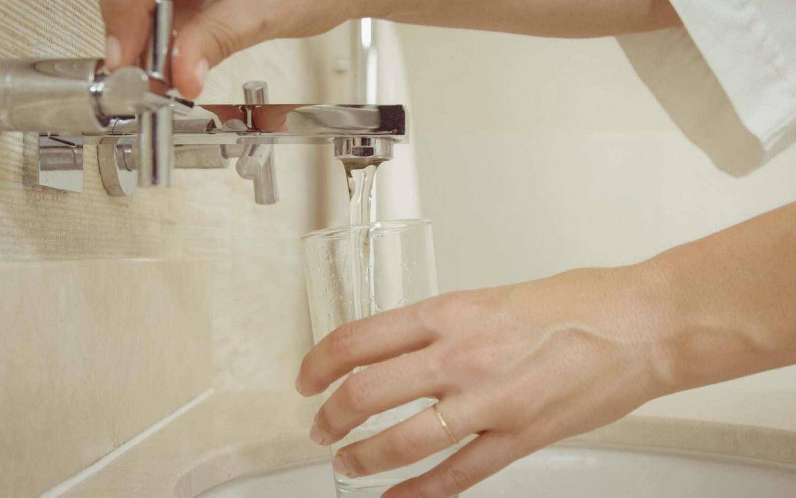 Ženska si toči v kozarec vodo iz pipe