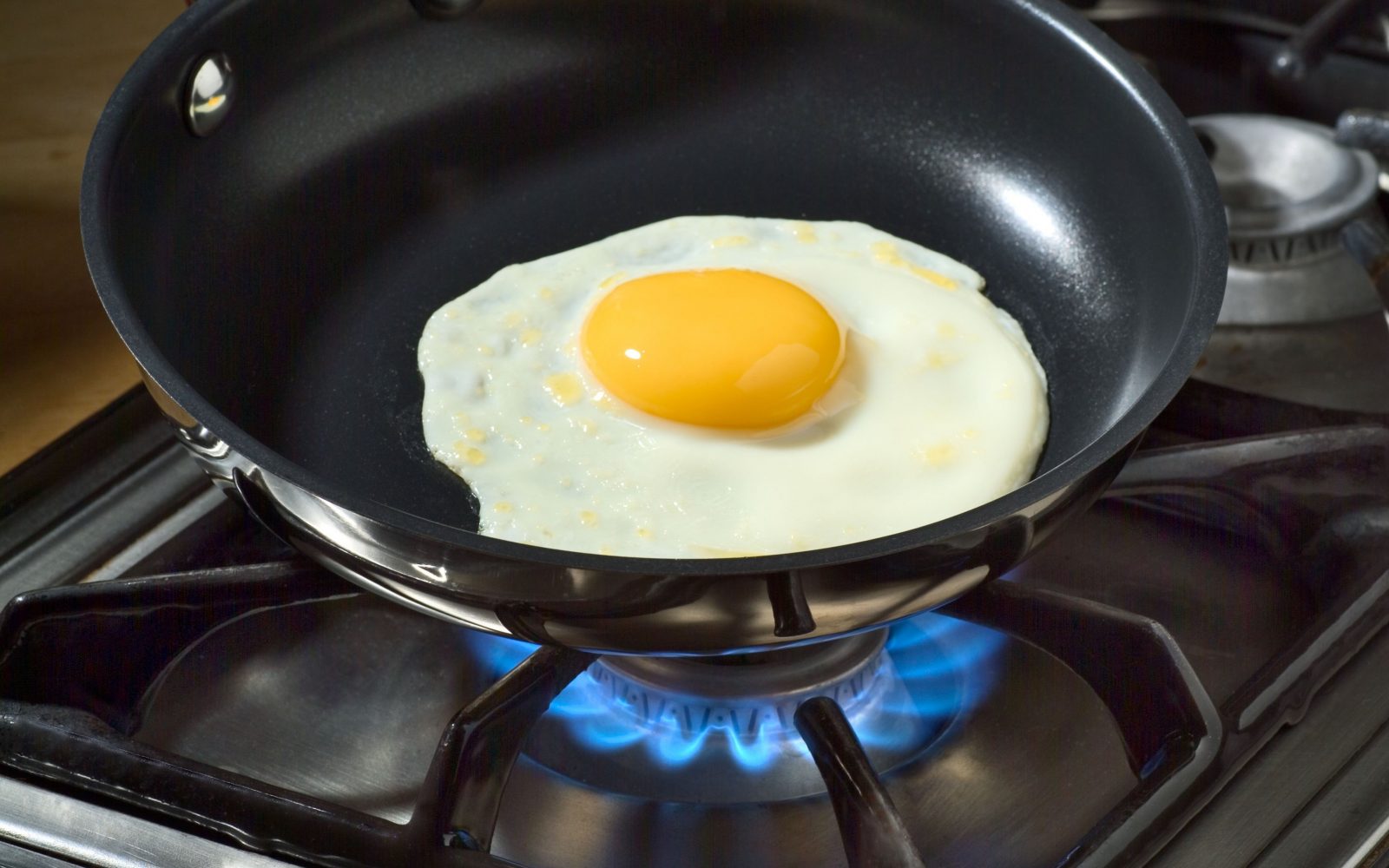 Fotografija prikazuje praženo jajce na ponvi, ki se kuha na plinskem štedilniku. Rumeno in belo jajce je popolnoma ocvrto, kar poudarja enostavnost in hitrost priprave okusnega zajtrka. Ta slika je idealna za članke o receptih za zajtrk, kuhanju jajc, zdravi prehrani in kuharskih nasvetih.