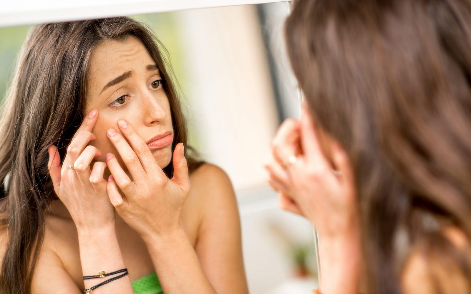 Mlada ženska se gleda v ogledalo, aknasta koža, aknavost
