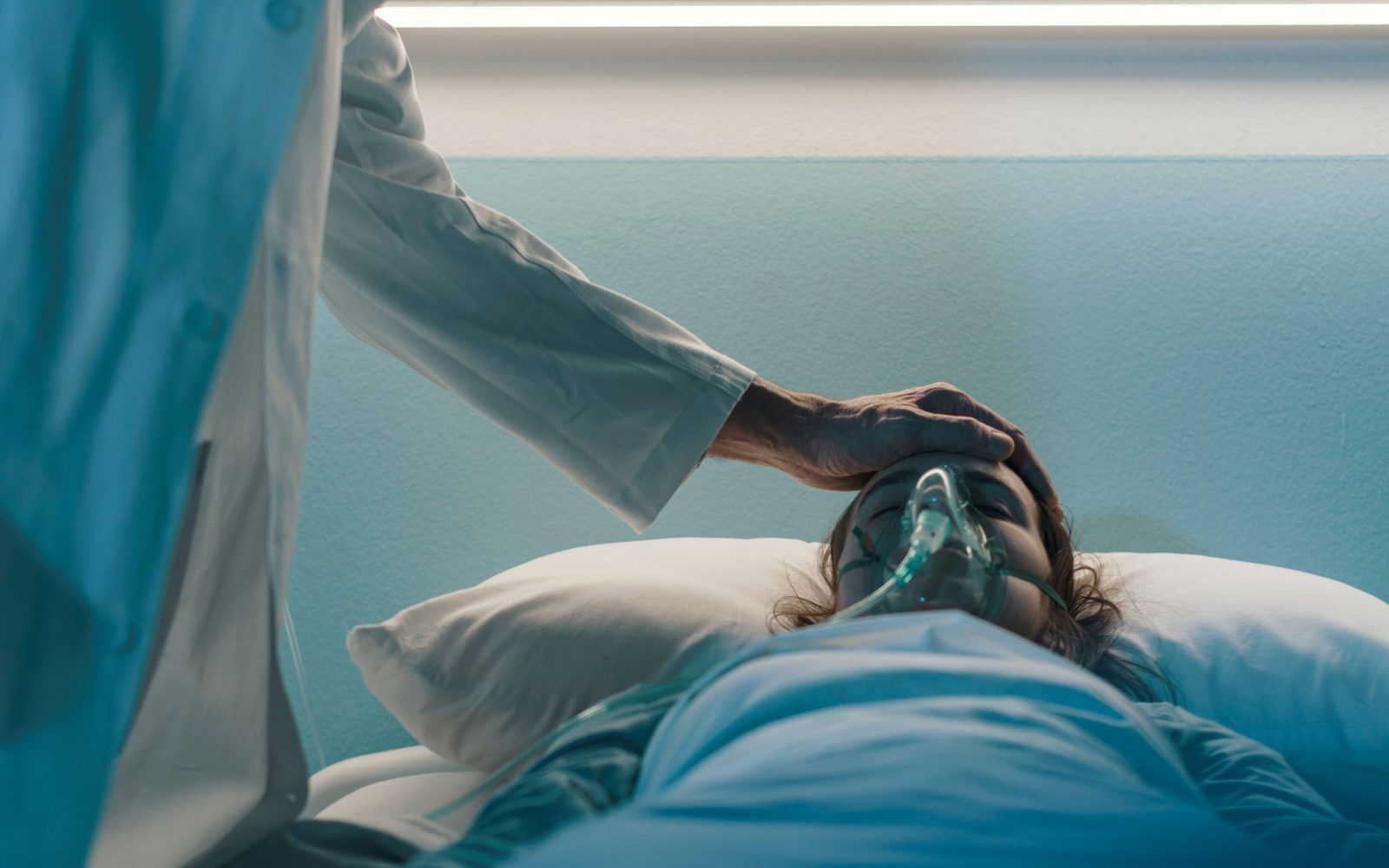 Ženska z respiratorjem leži v bolniški postelji