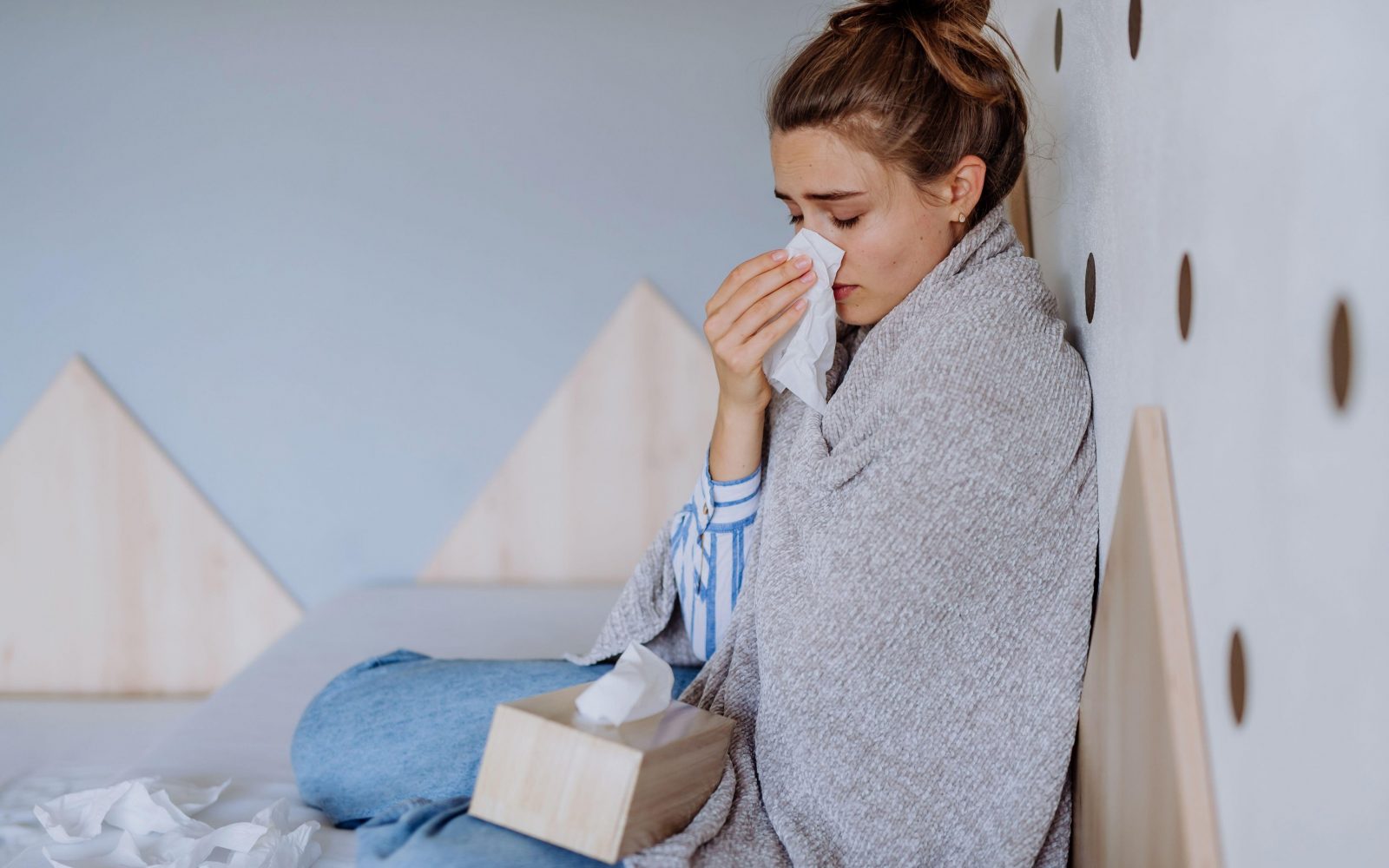 Ženska sedi ogrenjena in si briše nos, ker je prehlajena