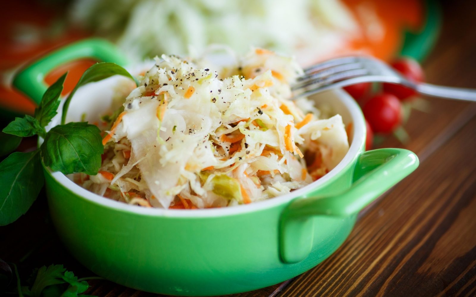 Sveže kislo zelje s korenjem in poprom v zeleni posodi, okrašeno z listom bazilike.