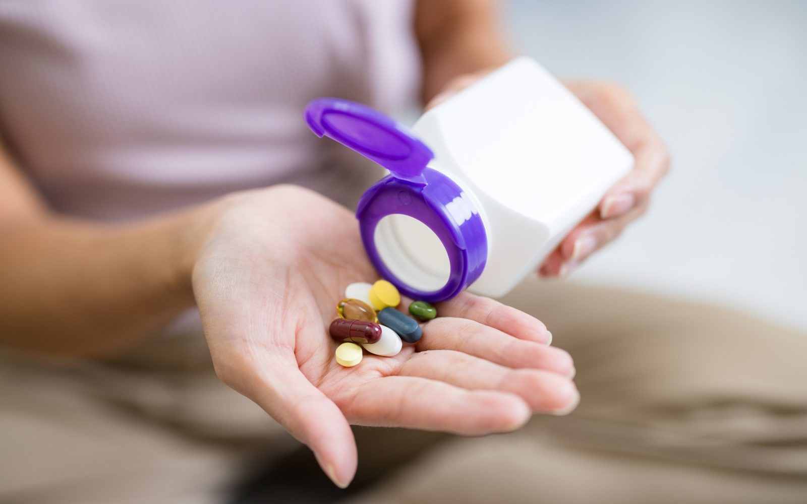 Oseba drži različne vitamine in prehranske dodatke v roki.