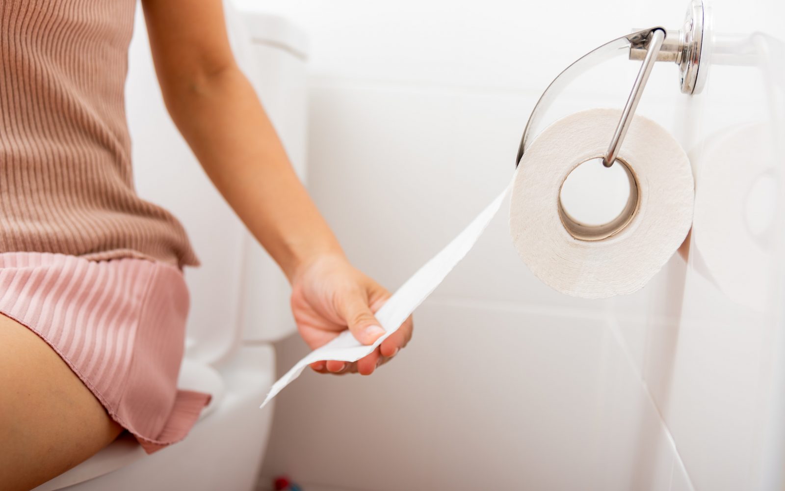 Ženska sedi na stranišču in drži toaletni papir