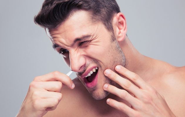 Moški odstranjuje nosne dlačice in se pri tem pači zaradi bolečin