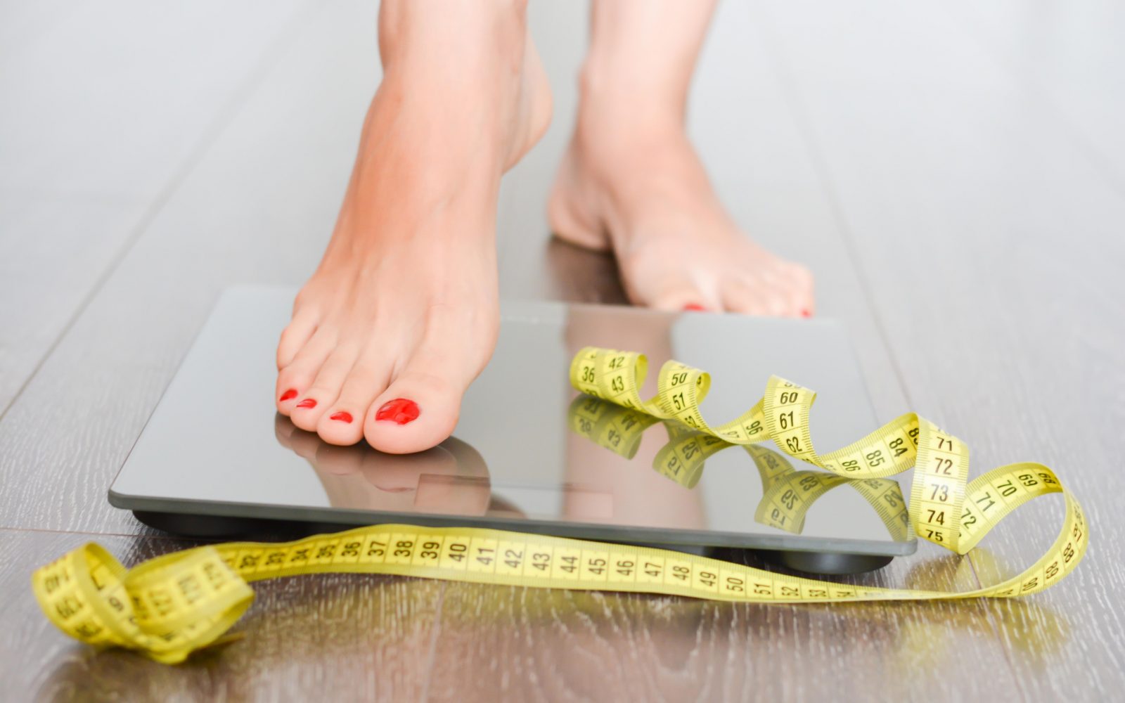 Ženska stopa na tehtnico, na kateri je merilni trak