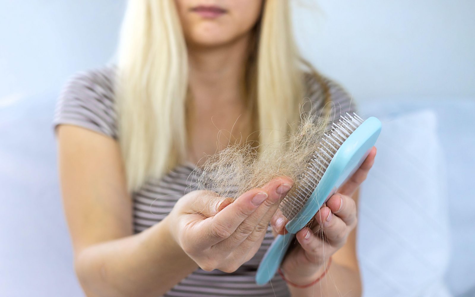 Ženska, ki se je počesala s krtačo, iz krtače pobira izpadle lase