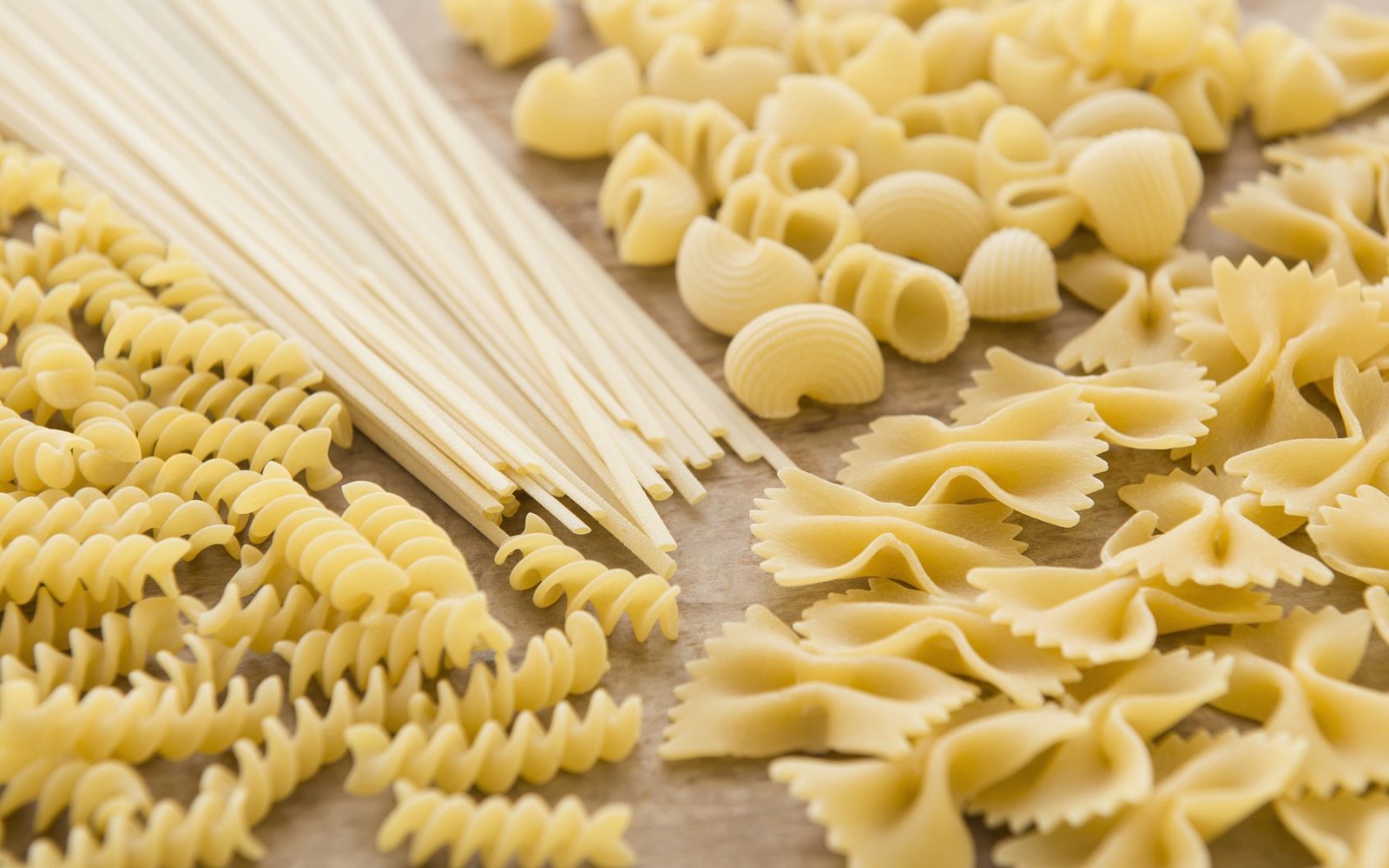 Različne vrste testenin, suhe testenine, fusilli, penne in rigatoni na lesenem ozadju.