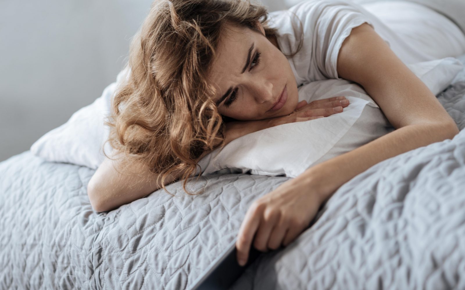 Žalostna ženska leži na postelji in v rokah drži telefon