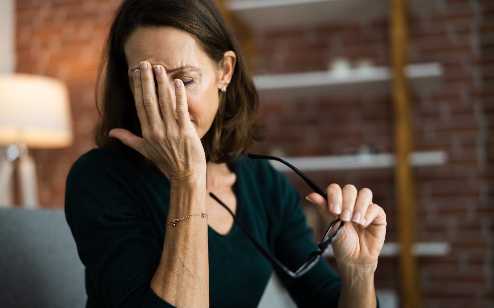 Utrujena ženska je snela očala in se drži za čelo, ker jo bolijo oči in glava