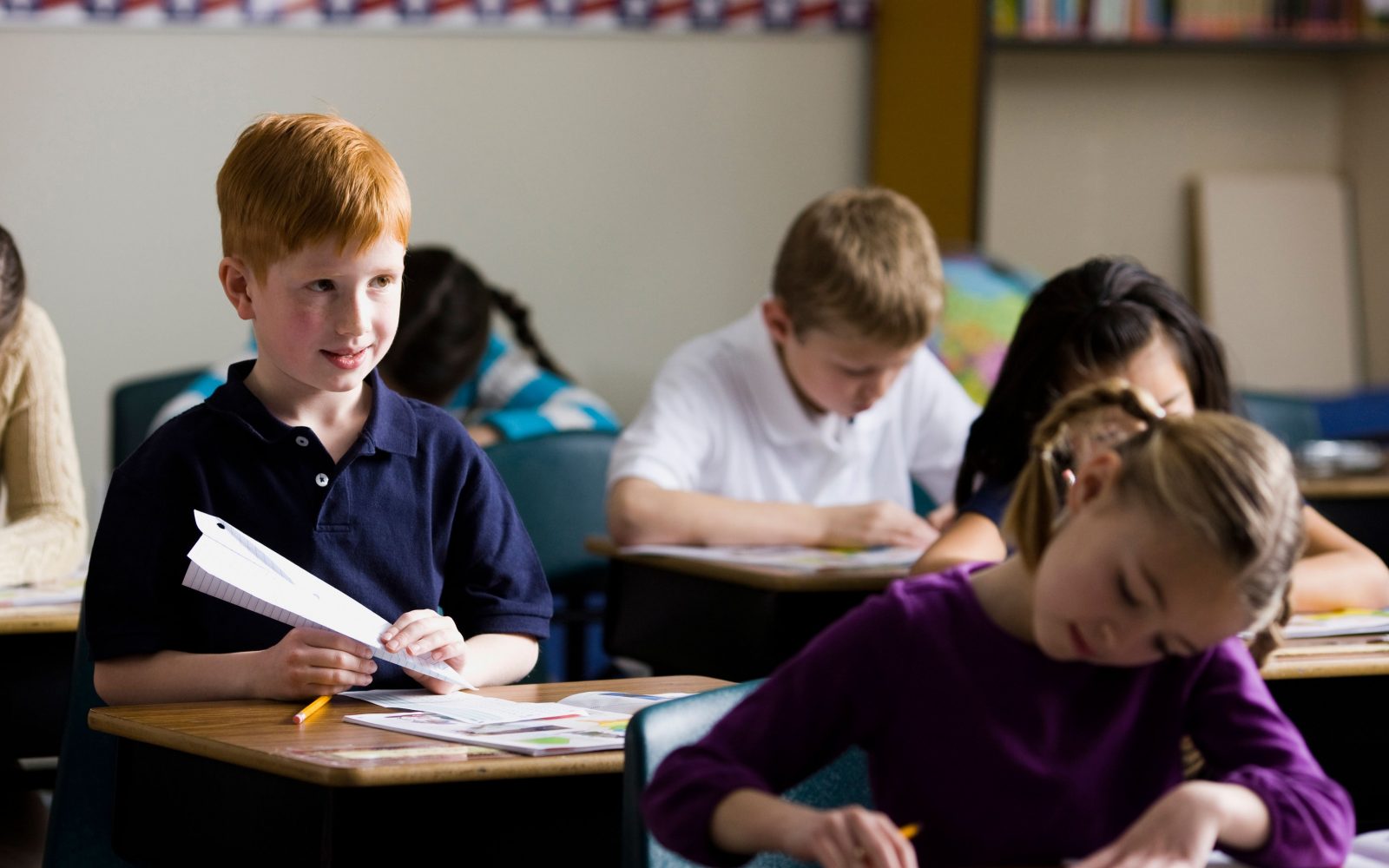 Otroci sedijo za šolskimi klopmi med poukom v razredu