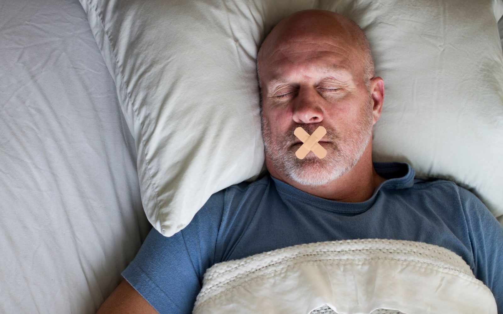 Moški spi z zalepljenimi usti – priljubljena metoda proti smrčanju in izboljšanju dihanja.