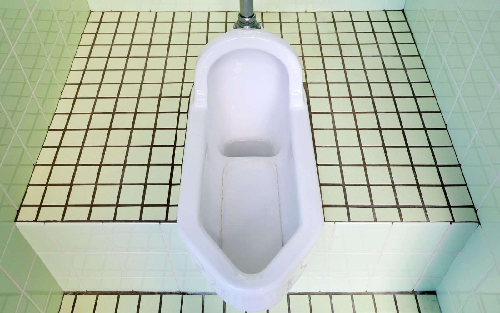 Tradicionalno japonsko stranišče na počep z belo keramično školjko in zelenimi ploščicami.