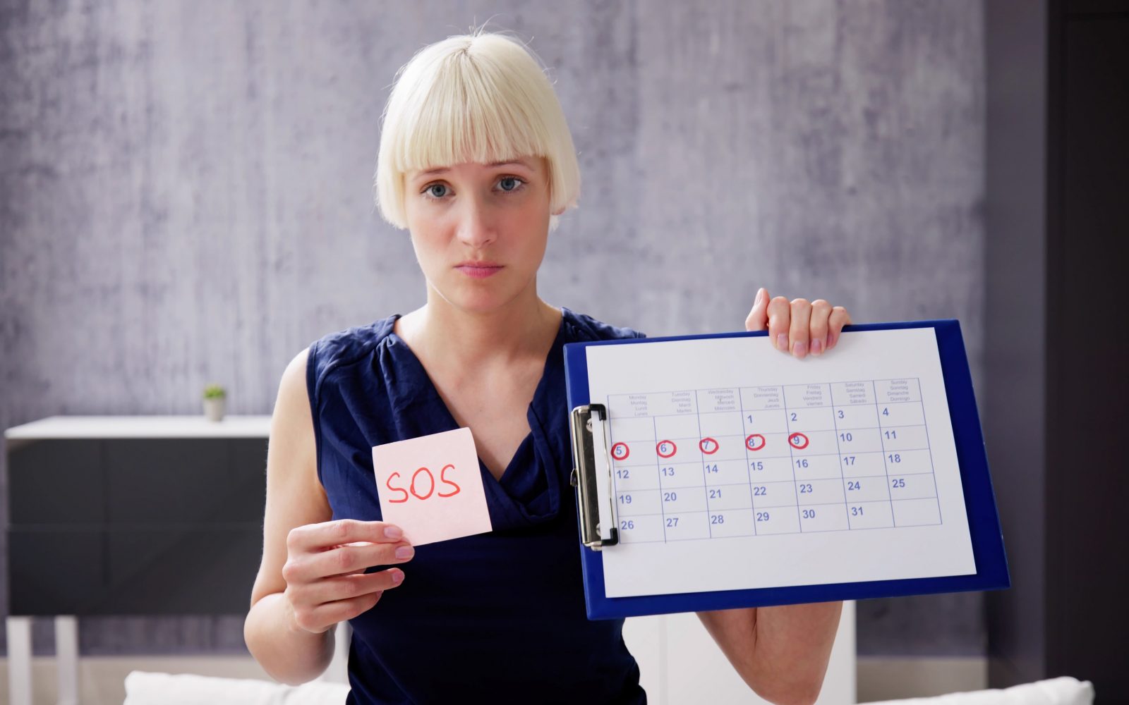 Ženska v rokah drži menstrualni koledar in znak SOS kot simbolični klic na pomoč