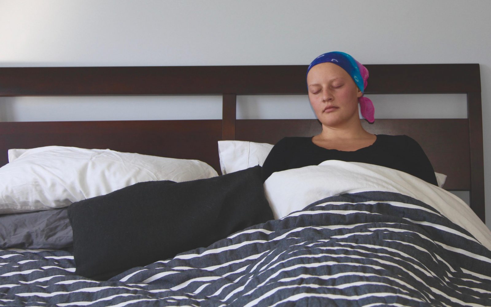 Bolnica z rakavo boleznijo, ki ima na glavi ruto, leži v postelji, utrujena