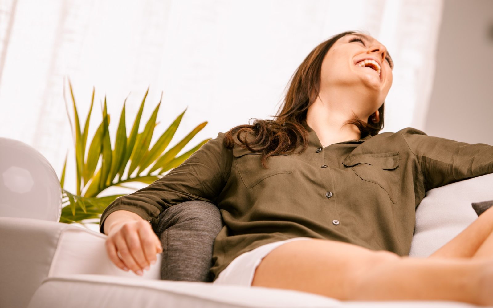 sproščena nasmejana ženska na kavču v domači sobi