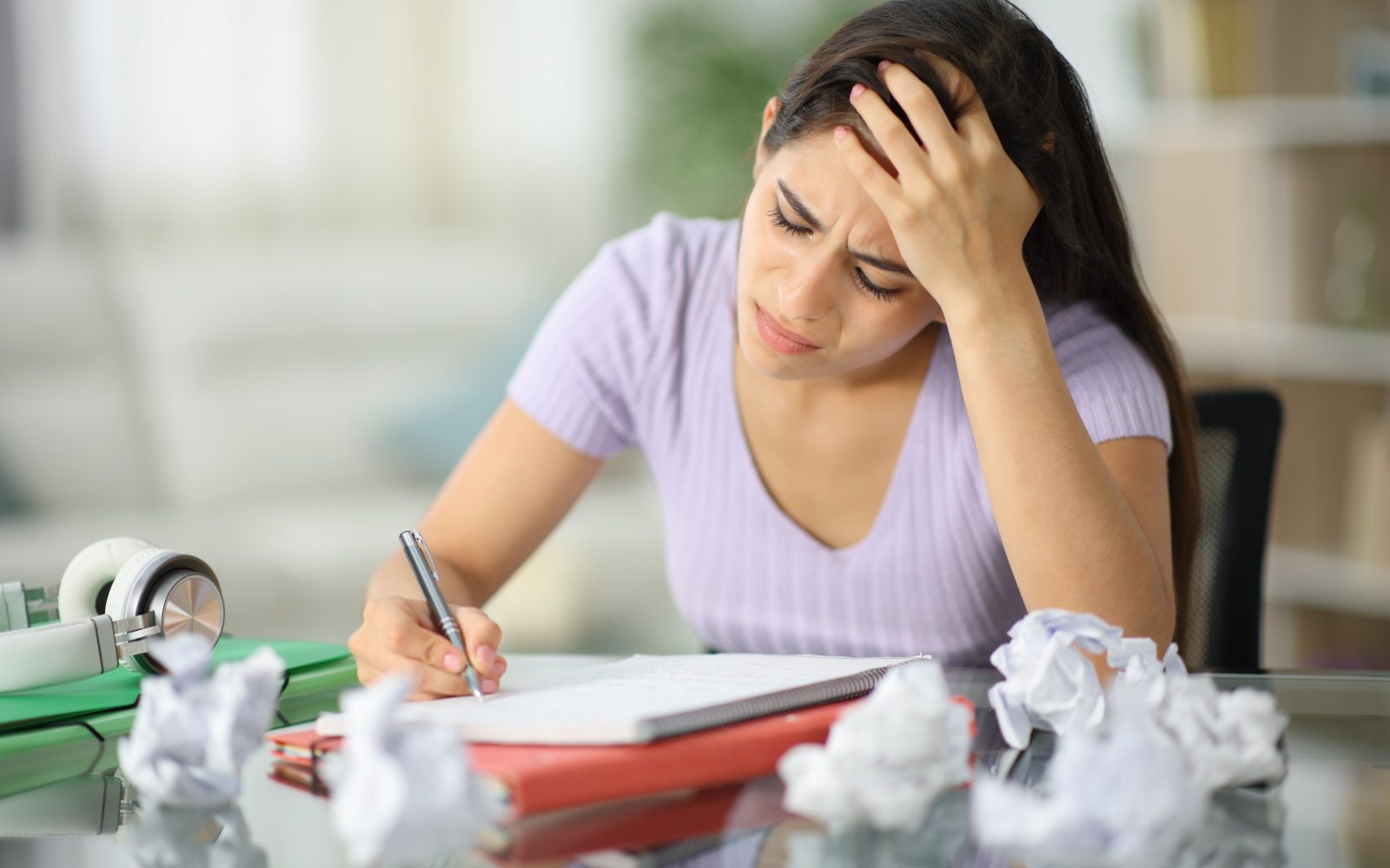 Slabovoljna študentka pod stresom, ki poskuša narediti nalogo pa ji ne gre. Na mizi je zmečkan papir in zvezek.