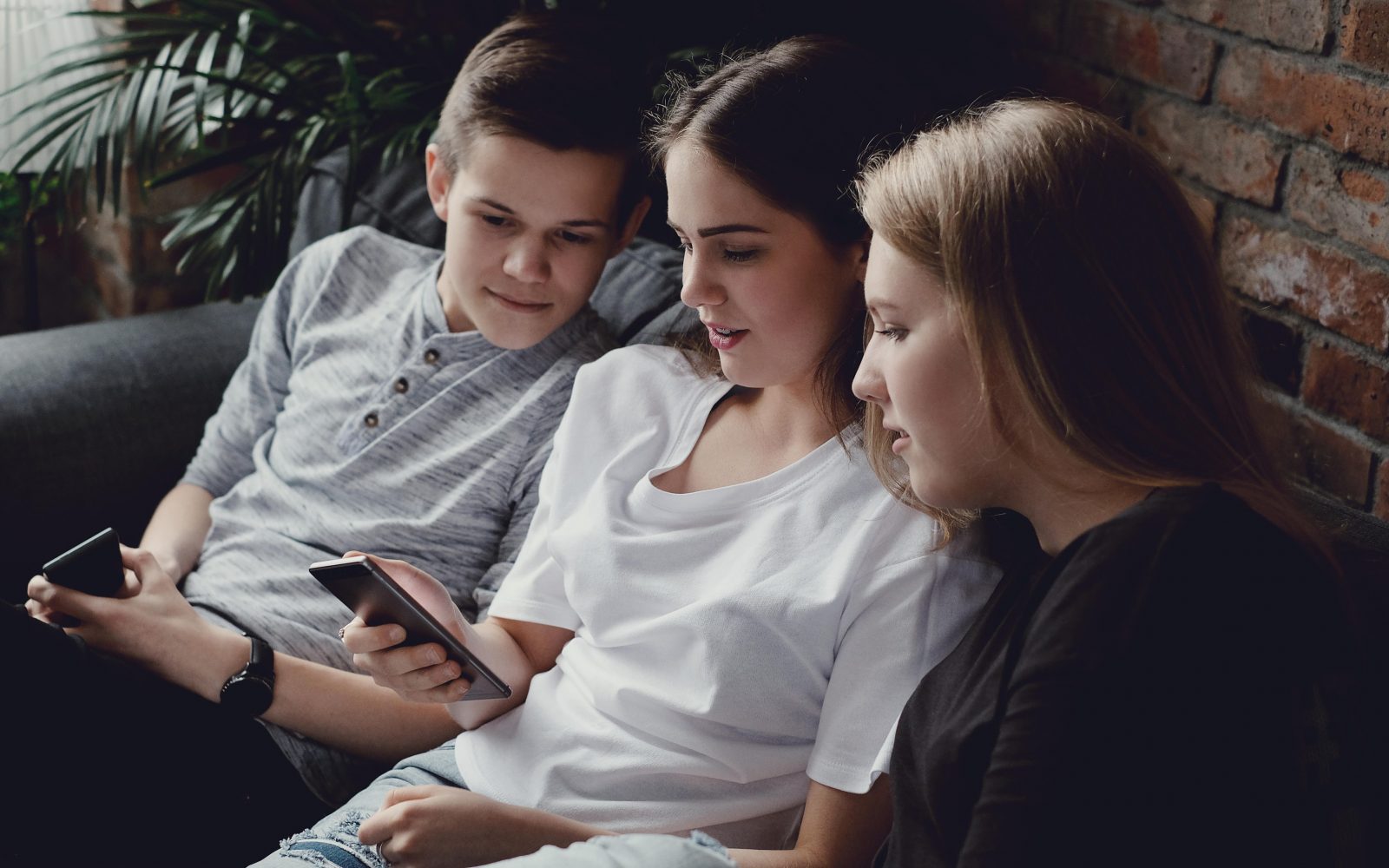 Dve najstnici in en najstnik gledajo v pametni telefon. Sedijo na kavču