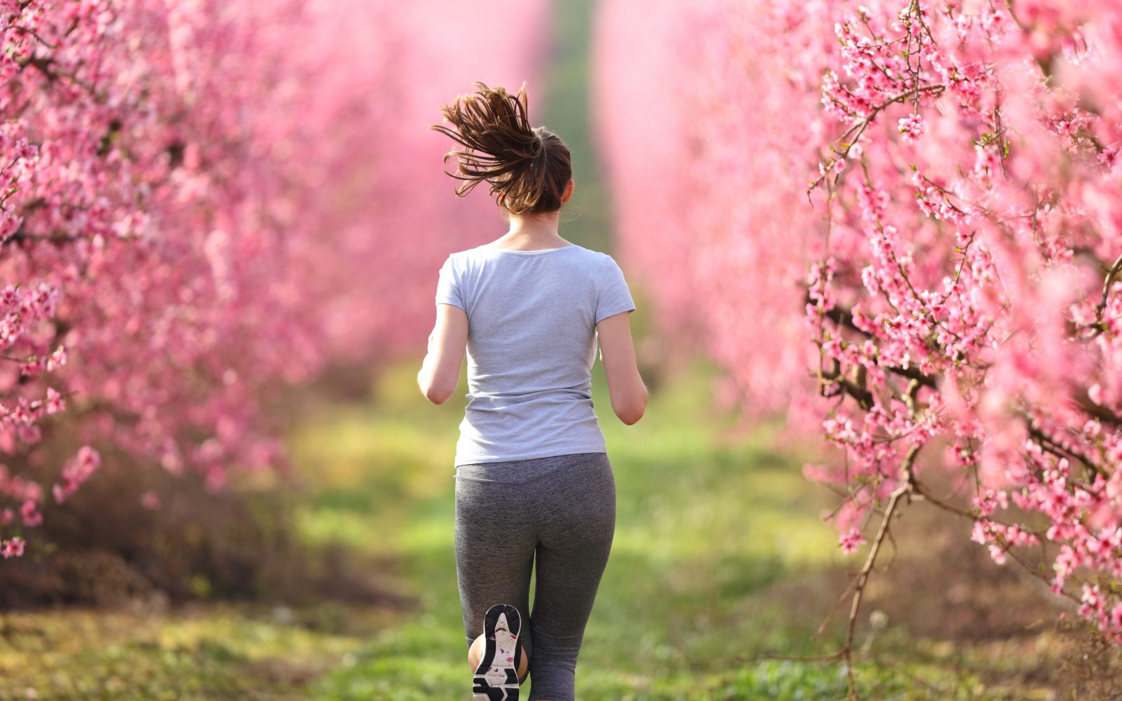Ženska teče v naravi, okoli nje cveti grmovje, pomlad