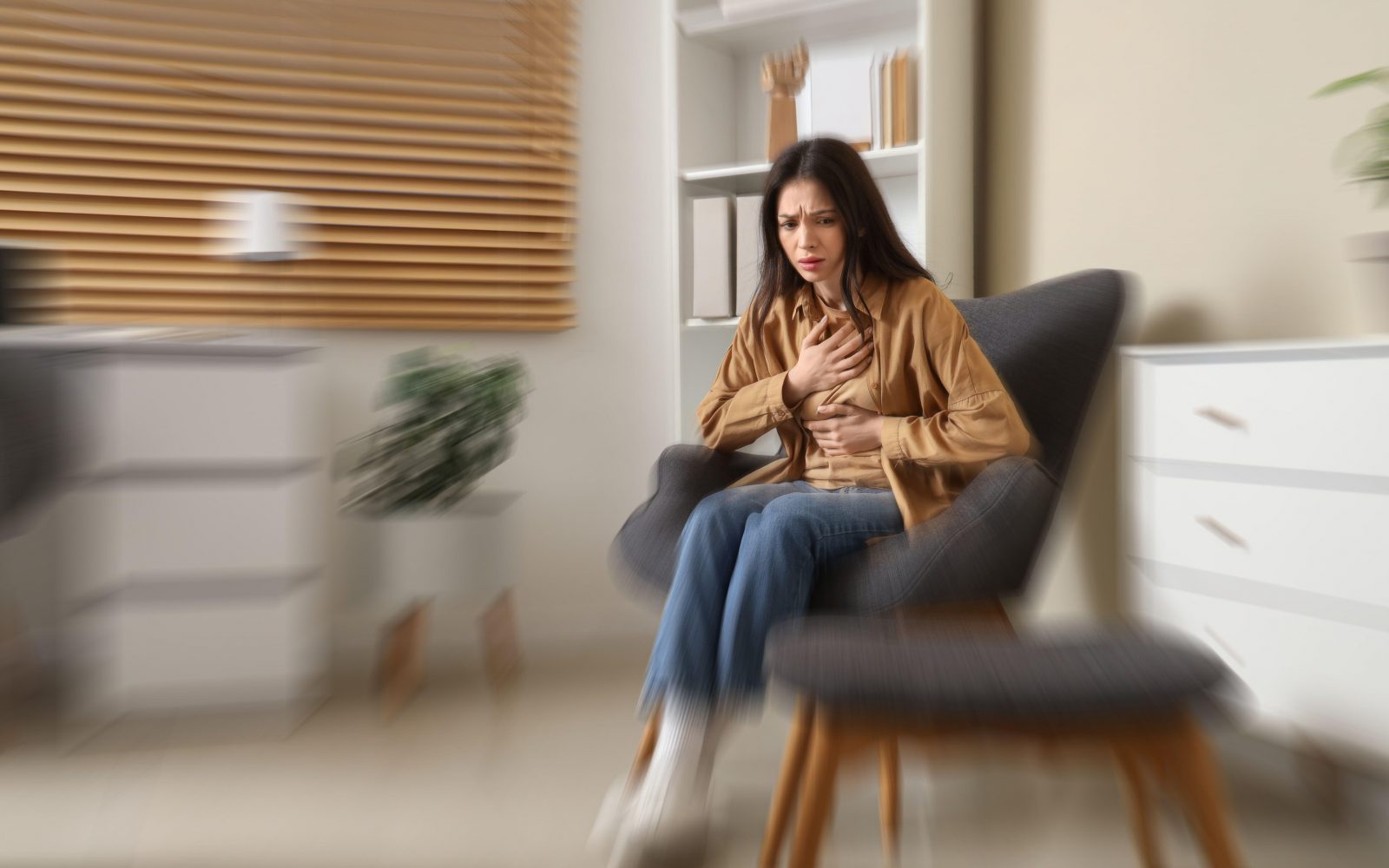 Mlada ženska ima napad panike ali hud napad tesnobe, medtem ko sedi v fotelju doma. Zaradi simptomov kot sta bolečina v prsih in nelagodje v želodcu se drži ima roki na trebuhu in prsnem košu.