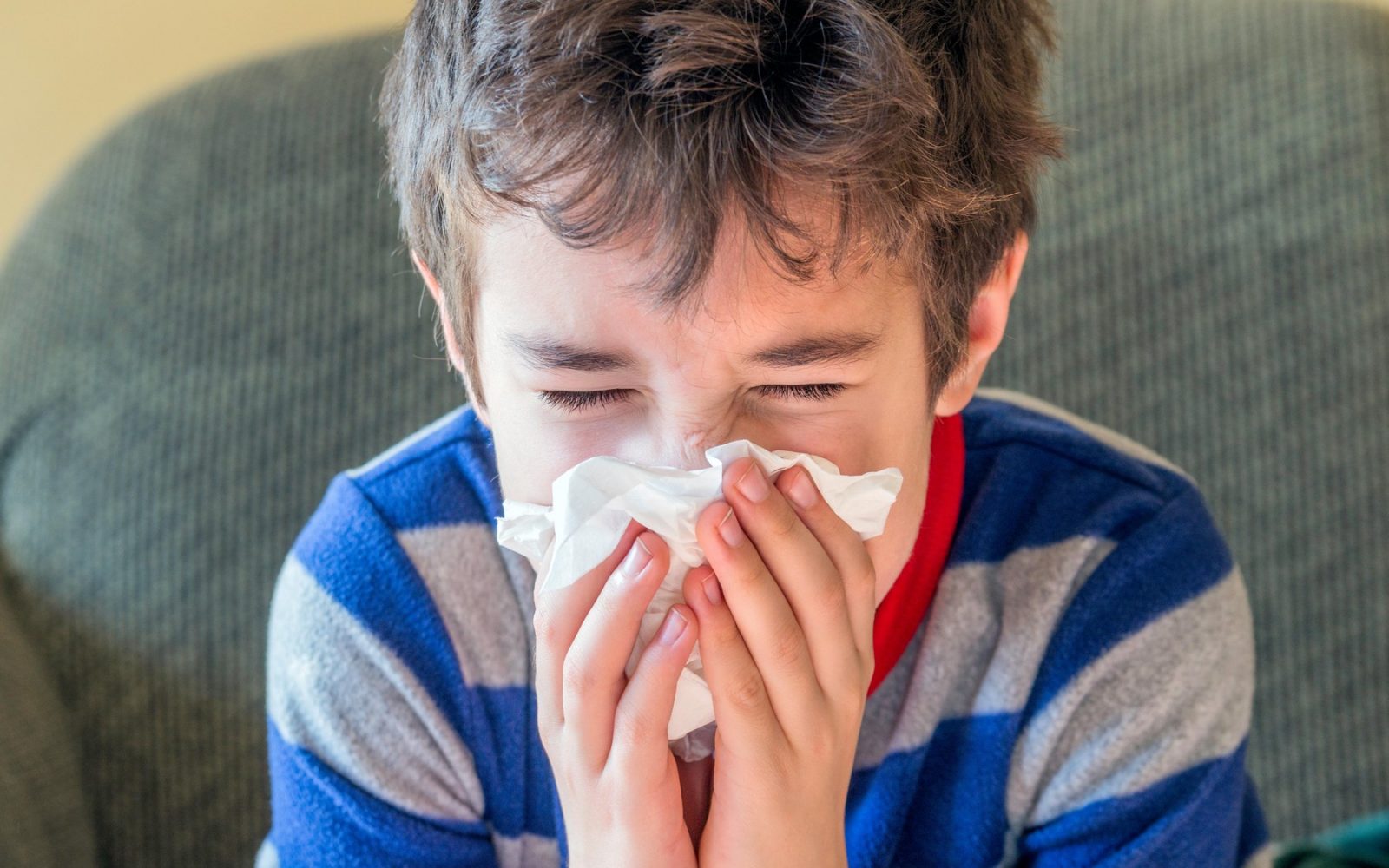 Mladi deček kiha v robček, medtem ko je doma bolan in v pižami – koncept zdravja ob prehladu in gripi.