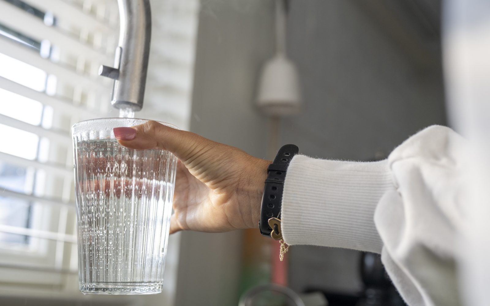 Ženska roka polni kozarec z vodo iz pipe – redna hidracija, pomembna navada za dobro počutje in duševno zdravje.