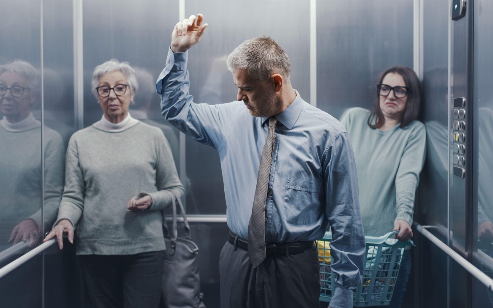 Moški s potnimi in smrdečimi pazduhami v natrpanem dvigalu, drugi ljudje ga zgroženo opazujejo in se z gnusom odmikajo.