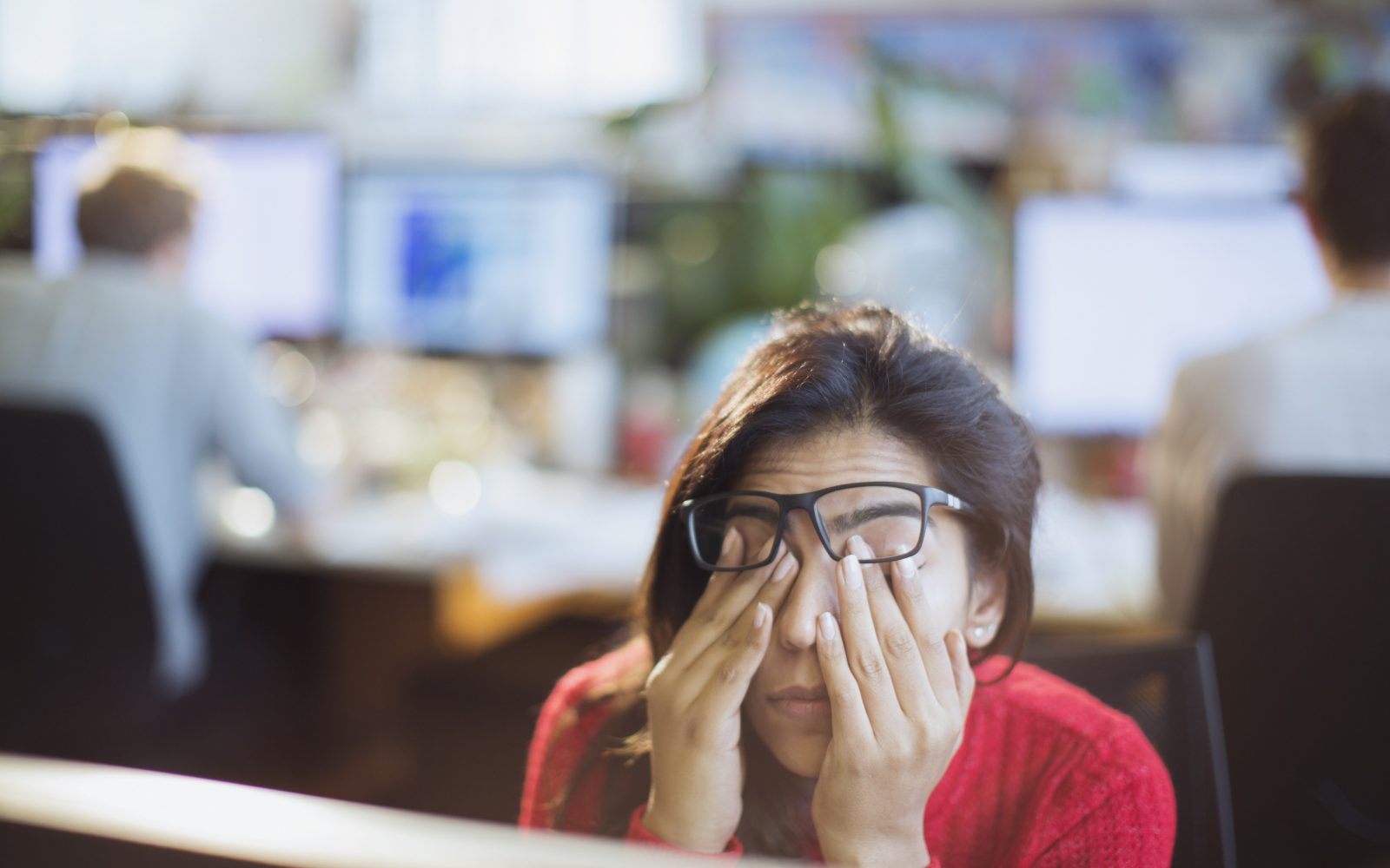 Ženska pod stresom na delovnem mestu si mane oči – stres kot pogost vzrok za hormonsko neravnovesje in neredne menstruacije.