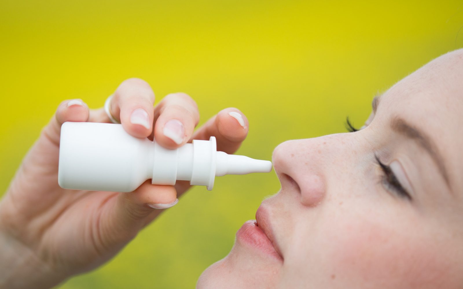 Ženska uporablja pršilo za nos za lajšanje simptomov sezonskih alergij, kot so zamašen nos in kihanje – pogosti znaki alergije na cvetni prah spomladi.